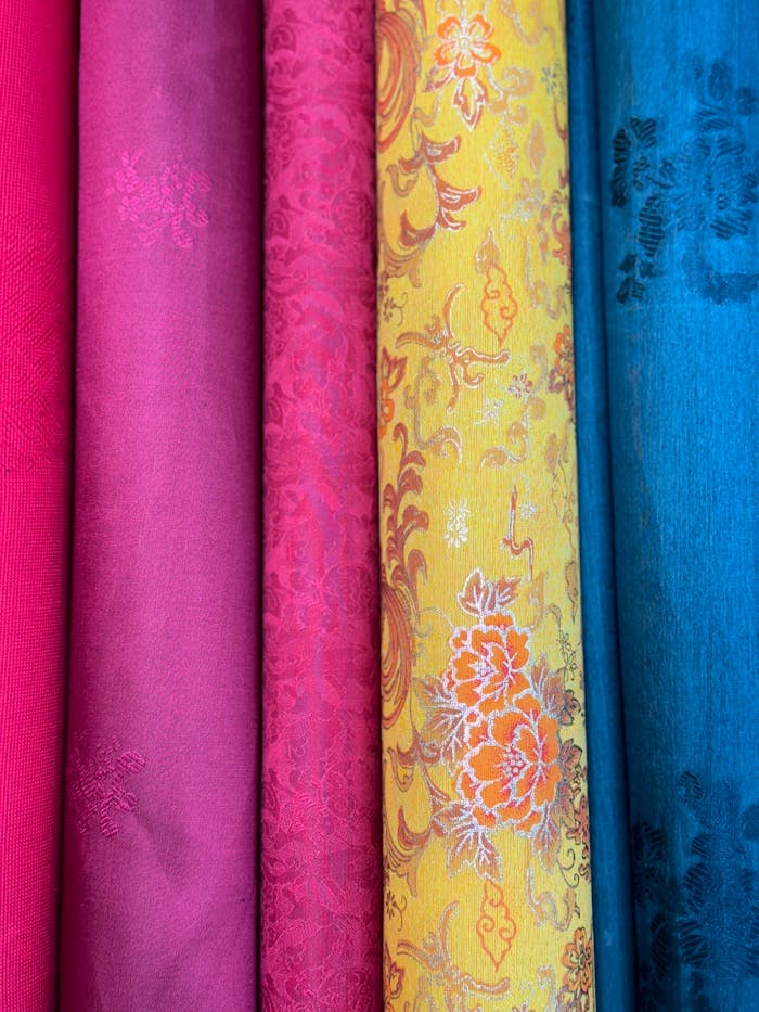 Vibrant textile rolls in pink, yellow, and blue with intricate patterns.